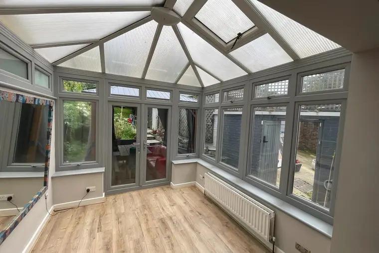 Inside a grey-framed conservatory with an old polycarbonate roof and roof vents, before replacement