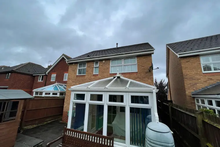 White Victorian conservatory with a polycarbonate roof behind a brick semi on an overcast day